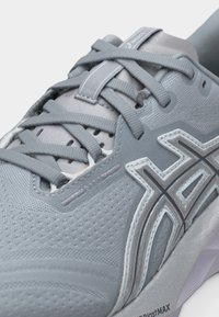 Κοντινό πλάνο ενός γκρι παπουτσιού τρεξίματος Asics που δείχνει την υφασμάτινη, υφή πάνω, τα κορδόνια και το λογότυπο στο πλάι.