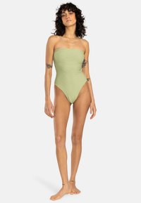 Maillot de bain une pièce sans bretelles en tissu côtelé vert clair ; design à jambe haute et détails de fronces sur les côtés ; texture lisse.