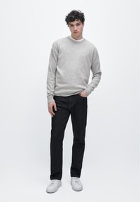 Maglione grigio chiaro, jeans scuri e sneakers bianche. Il maglione ha una semplice scollatura a girocollo e una texture morbida, mentre i jeans hanno una vestibilità classica.