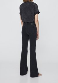 Jeans negros de campana con una cintura alta, diseño de cinco bolsillos y un ligero desvanecimiento. Combinados con una camisa negra de manga corta.