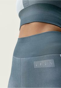 Stanik sportowy i legginsy z wysokim stanem w teksturowanym jasnoniebieskim materiale. Zawiera naszywkę z logo na pasie. Gładki, dopasowany krój.