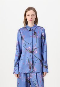 Γαλάζιο πουκάμισο με μακριά μανίκια, με εμπριμέ λουλουδιά σε μωβ και πράσινο. Διαθέτει αιχμηρό γιακά και κλείσιμο με κουμπιά στο μπροστινό μέρος.