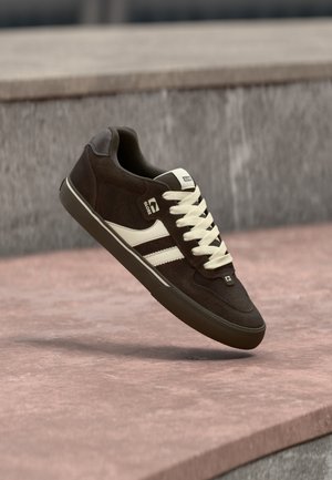 Brun og beige skate-sko med hvide snørebånd, sort sål og Globe-logo, der svæver over en lyserød betonoverflade.