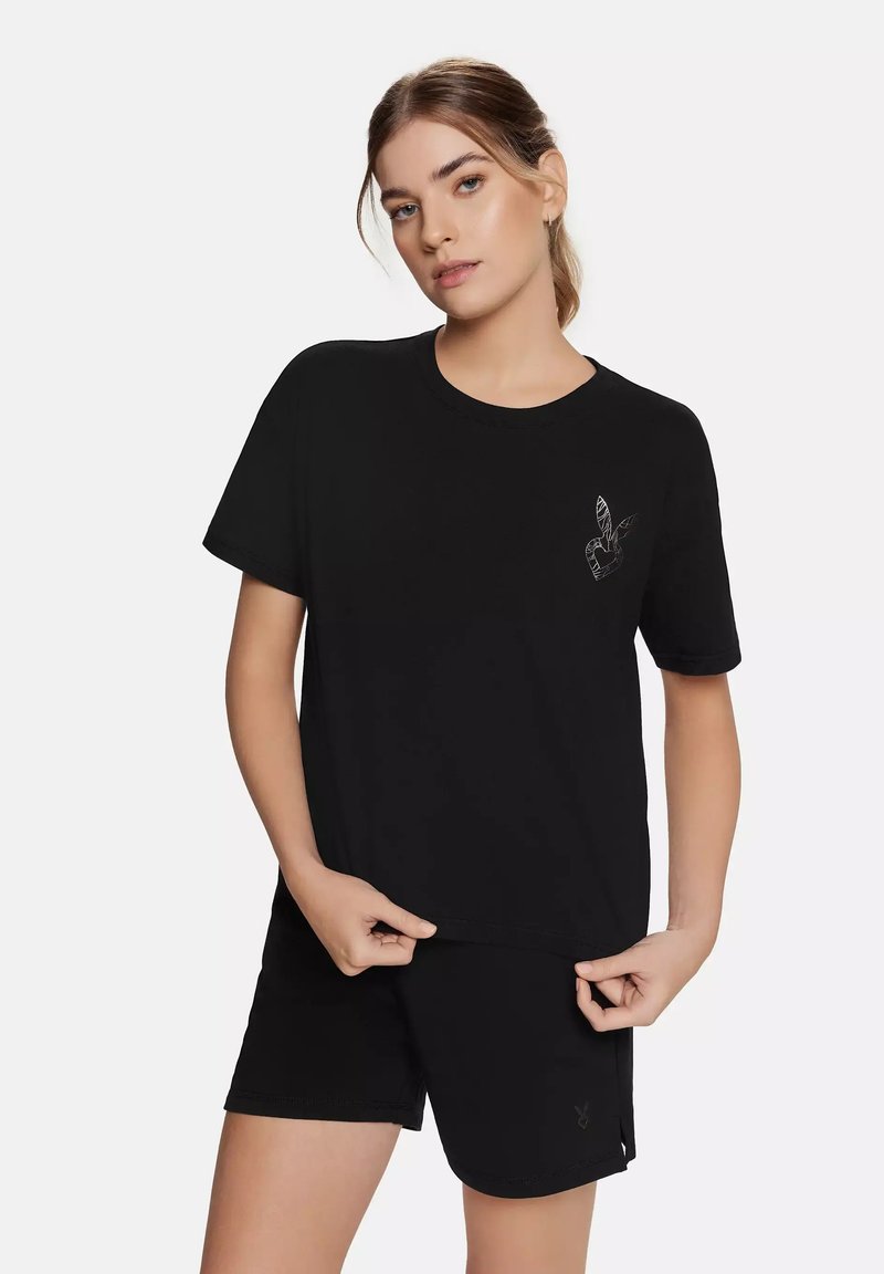 Sort bomulds t-shirt med kortærmer, rund halsudskæring, med et subtilt grafisk motiv på venstre bryst. Samlet med sorte shorts.