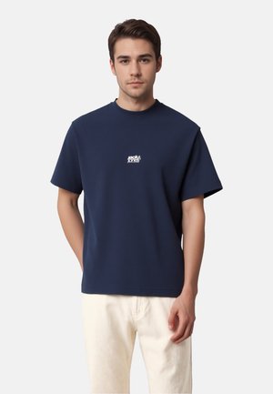 Mørkeblå bomuld T-shirt med rund hals og korte ærmer. Har en lille hvid logo på brystet og en afslappet pasform.