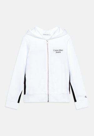 Sudadera blanca con cremallera y capucha, con acentos negros en los laterales y el logo "Calvin Klein Jeans". La tela es suave, lisa y de diseño casual.