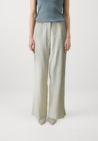 Pantalons larges en lin vert clair avec une texture lisse, dotés d'une fermeture éclair à l'avant et de détails de plis. Associés à des escarpins beiges à bout pointu.