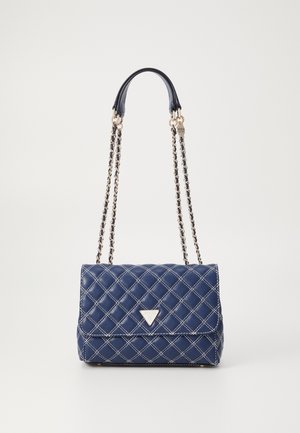 Sac à main matelassé bleu marine avec coutures blanches, fermeture à rabat, anses chaînes dorées et logo triangulaire Guess sur le devant.