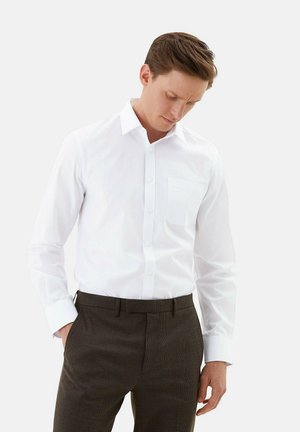 Camisa blanca de manga larga con cuello y bolsillo, combinada con pantalones de cuadros marrones. Tejido suave con un diseño entallado.