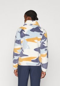 Fleece pullover in een camouflagestof met blauwe, gele en witte tinten. Heeft een hoge kraag en een gestructureerde stof voor warmte.