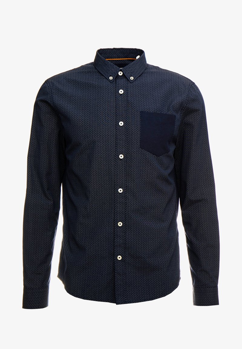 Camicia a maniche lunghe blu navy con un piccolo motivo a pois bianchi, colletto alla francese e una tasca a toppa scura sul lato sinistro del petto. Bottoni bianchi.
