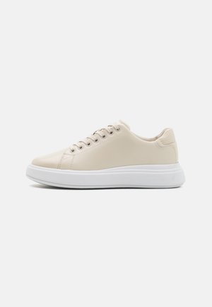 Baskets en cuir beige avec un bout arrondi, semelle en caoutchouc blanche et six œillets pour les lacets. Un accent texturé à l'arrière ajoute du détail.