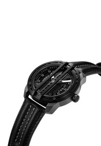 Svart analog klocka med en texturerad läderrem, rund boett, djärv svart urtavla, silverdetaljer och distinkt överliggande design.