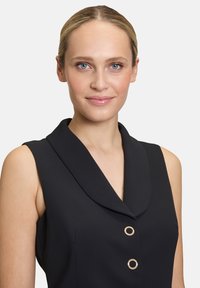 Czarna bezrękawnikowa sukienka z kołnierzem szalowym, ozdobiona dwoma okrągłymi guzikami w kolorze złota, wykonana z teksturowanej tkaniny.