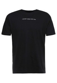 Svart bomullströja med korta ärmar, med vit text "JAG ÄR INTE HÄR FÖR DIG" över bröstet. Enkel rundhalsad design.