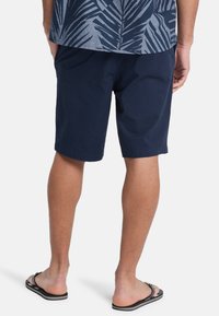 Marine korte broek van lichtgewicht stof, met een relaxte pasvorm en een nette zoom. Gepaard met zwarte slippers, gezien van achteren.