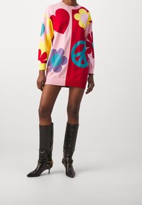 Vestito lavorato a maglia colorato con sezioni rosa, rosso, giallo e blu, con motivi a cuore, fiore e simbolo della pace. Maniche lunghe e orlo a coste.