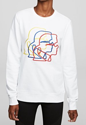 Sweat-shirt blanc à manches longues avec des contours multicolores superposés de quatre visages portant des lunettes de soleil sur la poitrine, porté par une personne.