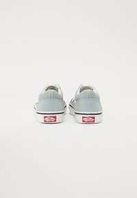 Sneakers in suede azzurro chiaro con suole bianche, la vista posteriore mostra un logo nero e rosso sul tallone. Design classico low-top con dettagli cuciti.
