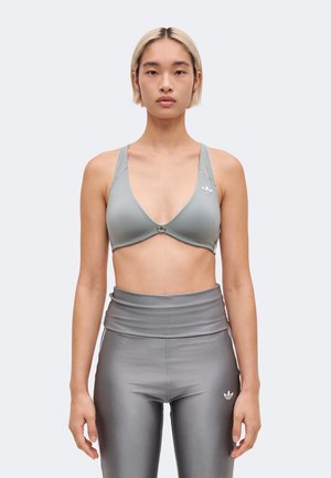 Un mannequin portant une brassière de sport grise et un legging taille haute se tient devant un fond uni clair.