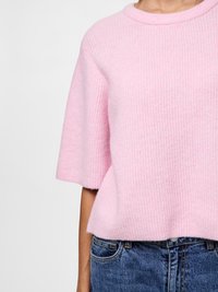 Camisola de malha rosa claro com mangas curtas, decote redondo e textura canelada. Combinada com jeans de ganga azul escuro.