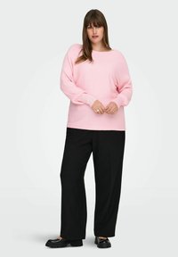 Lys rosa ribbestrikket genser med bred hals og lange ermer; kombinert med svarte vide bukser og svarte loafers. Myk tekstur.