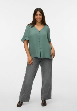 Blouse verte à manches courtes avec décolleté en V, fermeture à boutons sur le devant et manches volantées. Associée à un jean gris à taille haute et à jambes larges.