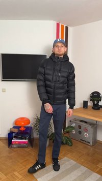 Μαύρο μπουφάν με κουκούλα και ορατές τσέπες με φερμουάρ, σε συνδυασμό με ναυτικές μπλε παντελόνα και μαύρα αθλητικά παπούτσια με λευκές ρίγες.