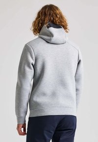 Felpa con cappuccio grigia chiara in tessuto texturizzato, vestibilità comoda e tasca a marsupio. Presenta una fodera scura in contrasto all'interno del cappuccio.