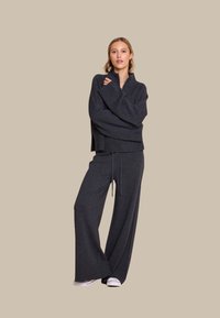 Mørkegrå, oversized genser med lange ermer, kombinert med bukser med brede ben. Begge plaggene har en myk tekstur og en uformell design. Hvite joggesko.