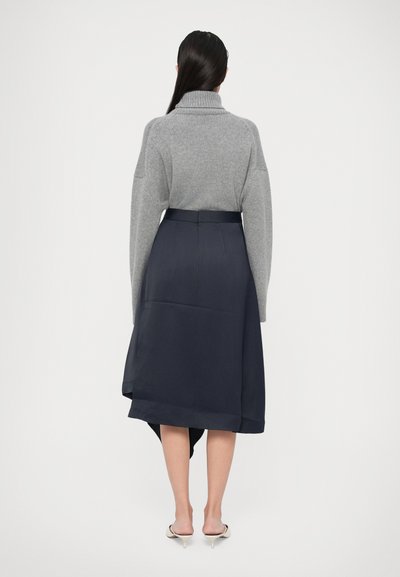 Maglione grigio a maglia con colletto alto, abbinato a una gonna asimmetrica blu scuro con una texture liscia e lunghezza sotto il ginocchio.