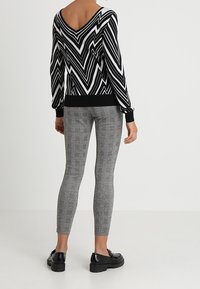 Schwarzer und weißer Sweater mit Zickzackmuster und V-Ausschnitt, kombiniert mit grauen Karo-Leggings. Schwarze Plateau-Schuhe runden das Outfit ab.
