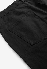 Sort denimstof med et nærbillede af en baglomme syet på tøjet, der fremhæver tekstur og sømdetaljer.