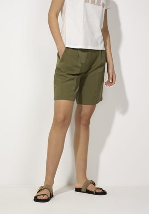 Shorts vert olive à coupe décontractée, dotés de poches latérales et d'un tissu texturé. Assortis à des sandales plates à bout ouvert.