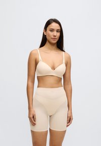 Sutien bej din material neted, cu bretele reglabile, asortat cu pantaloni scurți modelatori cu talie înaltă, fără cusături, în aceeași nuanță.