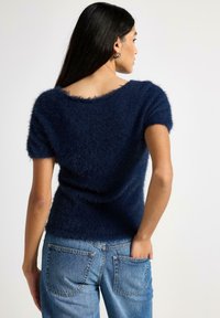 Navyblå kortærmet, blød sweater med bred halsudskæring og tekstureret finish, kombineret med lyseblå jeans med baglommer.