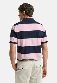 Polotröja i rosa och marinblå ränder med krage, korta ärmar och avslappnad passform; bärs med ljusa byxor och ett bälte.