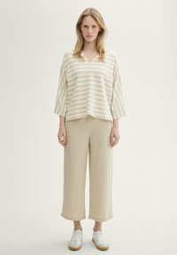 Haut à rayures beige et blanches avec un col en V et des manches trois-quarts, associé à un pantalon large en lin beige et des baskets blanches avec des accents marron.