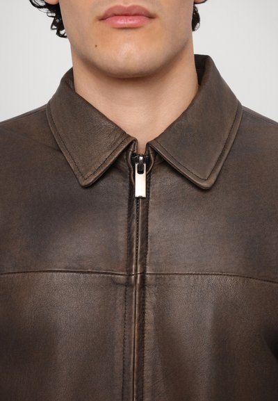 Bruine leren jas met een kraag, rits aan de voorkant met een zilveren trekker en zichtbare stiksels. Glad oppervlak, getailleerd ontwerp.