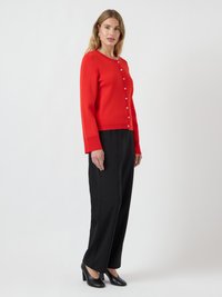 Rote Strickjacke mit Rundhalsausschnitt und Knopfverschluss vorne. Kombiniert mit schwarzen hochgeschnittenen Hosen und schwarzen High Heels.