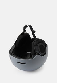 Pelēks ķivere ar gludu virsmu, regulējamiem melniem siksnām, mīkstu iekšpusi, ausu aizsardzību un ventilācijas atverēm sānos.