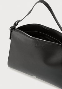 Geantă neagră din piele cu finisaj texturat, prevăzută cu fermoar în partea de sus și o curea reglabilă. Branding subtil pe partea din față.