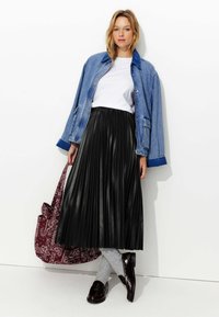 Veste en jean, t-shirt blanc, jupe plissée noire, chaussettes grises, chaussures sombres brillantes et sac fourre-tout maroon à motifs. Look simple et superposé.