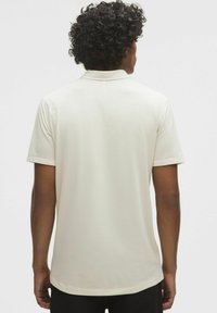 Korte mouwen poloshirt in lichtbeige, met een gladde textuur, heeft een klassieke kraag en een subtiele ribbelpatroon op de achterkant en mouwen.