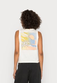 Camiseta sin mangas de algodón blanco con un gráfico colorido de un atardecer y una palmera en la parte de atrás. Corte recto con un ajuste relajado.