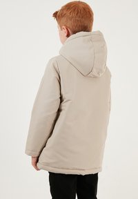Beige huva jacka med en slät yta, med en något överdimensionerad design och sömnadsdetaljer vid fållen.