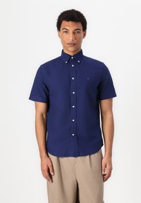 Camicia a maniche corte, con bottoni, in cotone navy con colletto classico. Presenta bottoni bianchi e un piccolo logo sul petto. La camicia è aderente.