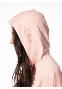Lichtroze hoodie met een gestructureerde afwerking, voorzien van een geborduurde boodschap in koraal op de zijkant, en een ruime pasvorm met een capuchon.