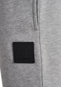 Grå sweatshirt tyg med en texturerad yta, med en svart rektangulär patch med präglad logotypdesign och sidofickor.