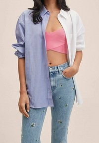 Chemise à bouton en rayures bleu et blanc, associée à un crop top en côtes rose et un jean léger bleu orné de motifs floraux.